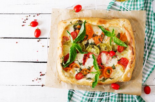 Mozzarella, tomatoes, basil savory pie on a white wooden background. Delicious food, appetizer in a mediterranean style. Top view. Flat lay