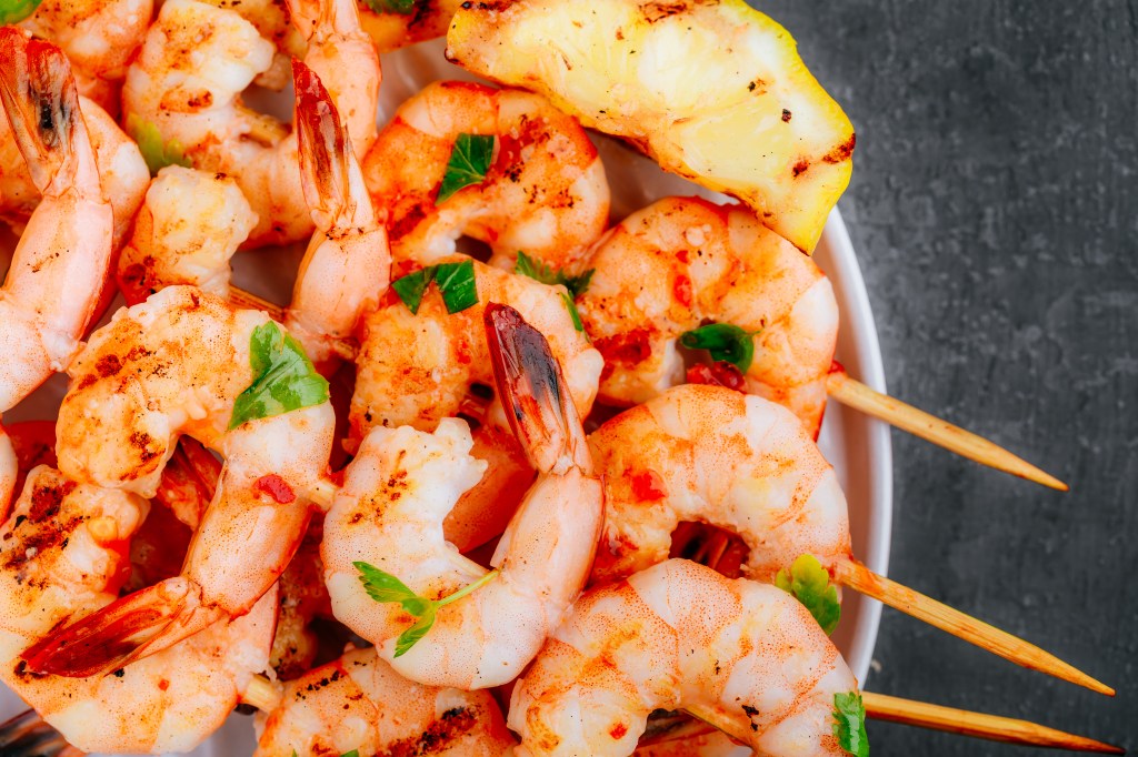 Grilled Lemon Shrimp Skewers in plate on gray stone background close up.