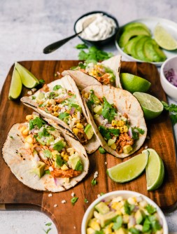 High angle of soft tacos with chicken, corn, avocado and lime.