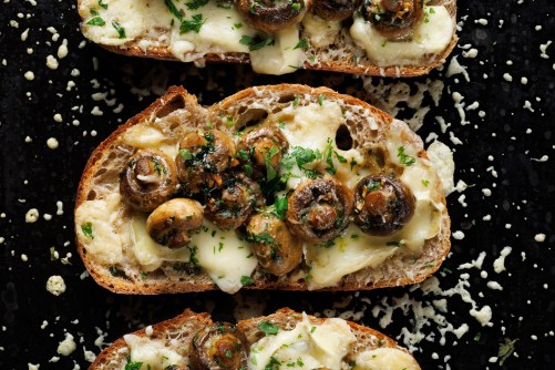 Grilled mushroom toast with cheese and herbs on a black background, close up