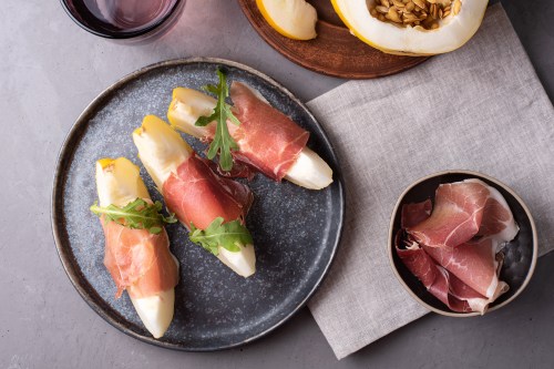 Italian ham and juicy melon appetizer, prosciutto with fruit on gray concrete background.